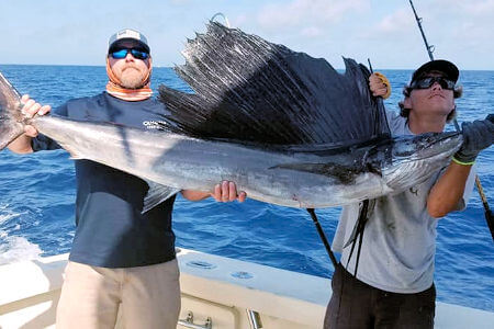 Mate and customer holding up Atlantic Sailfish before releasing it.
